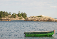 green aluminum boat anchored in water with smooth rock face behind